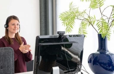 Lady communicating behind a computer using sign language.