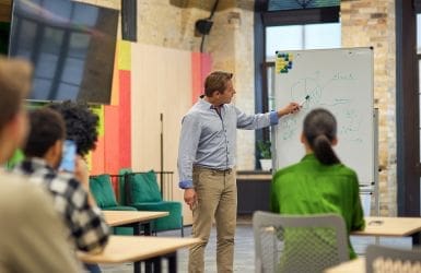 man met een whiteboard die iets uitlegt voor een klas