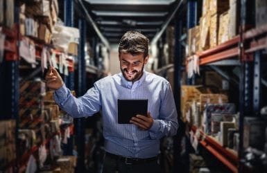 man in magazijn kijkt op zijn tablet