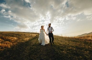 bruidspaar in trouwkleding loopt hand in hand in een veld
