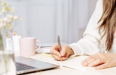 Vrouw, onherkenbaar in beeld, werkend achter een laptop.
